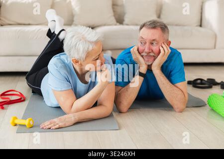 Fitness workout home training. Senior adult mature healthy fit couple resting after sports exercise on yoga mat at home. Mid age old husband wife have training workout. Health care healthy lifestyle Stock Photo