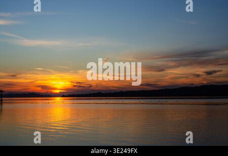 Sunset with dramatic colorful clouds, water and skies. Beautiful, colorful wispy skies with reflections on the water. Stock Photo