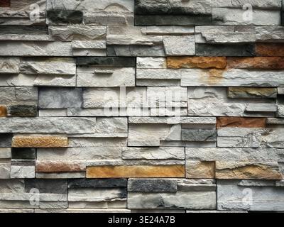 A textured wall surface made of stacked natural stone tiles in grey, white, and earthy brown tones for interior or exterior architectural design Stock Photo