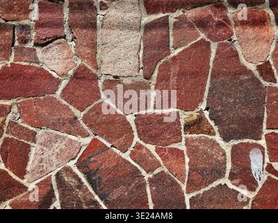 A textured wall surface made of irregular red and brown stone pieces held together by mortar Stock Photo