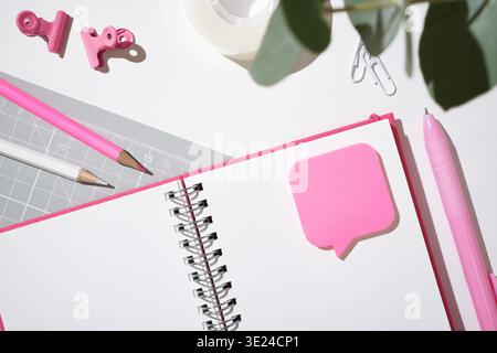 Pink stationery flat lay with open notebook with sticky note, paperclips and pencils on white desk. Copyspace Stock Photo