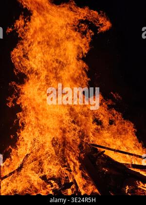 Bright orange flames leap and dance in a roaring fire, capturing the warmth, intensity, and dynamic energy of burning wood or a bonfire. Stock Photo