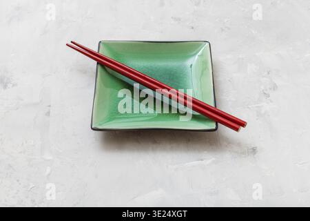 One green square saucer with red chopsticks on gray concrete surface Stock Photo