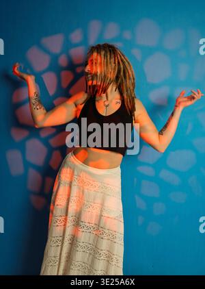 Young woman with dreadlocks smiling and dancing against an abstract patterned blue background Stock Photo