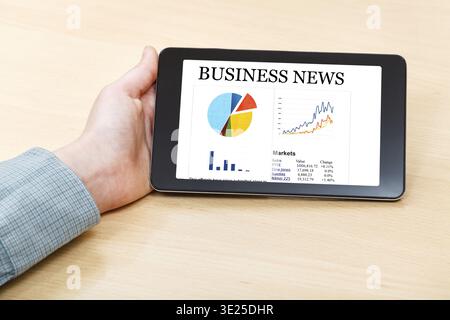 Businessman hand hold tablet PC with business news on screen at office desk Stock Photo