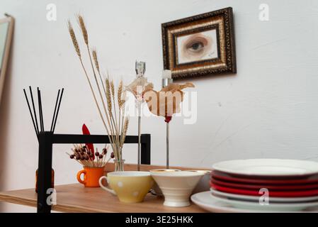Moscow, Russia - December 11, 2025 - Wooden table set with stacked plates, bowls, cups, reed diffuser sticks, matches in an orange mug, tall candle ho Stock Photo