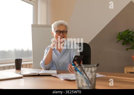 Confident middle aged senior woman euphoric winner with smartphone. Older mature lady looking at cell phone reading great news getting good result winning online bid feeling amazed. Winning gesture Stock Photo