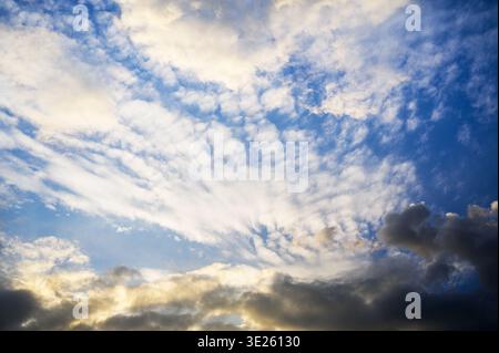 Dramatic sky with wispy clouds and golden sunlight breaking through dark storm clouds Stock Photo