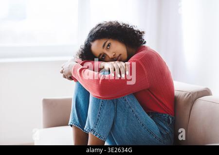 Woman Sitting on a Couch, Resting Her Head on Her Knees in a Bright Room During the Day Stock Photo