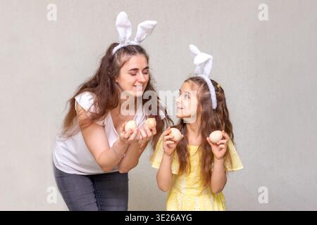 Mother and daughter wearing bunny ears holding Easter eggs and sharing a joyful spring moment Stock Photo
