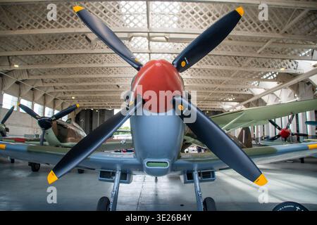 IWM Duxford Summer Airshow - Front-facing view of a vintage single-engine fighter plane with a large propeller and red spinner, parked inside an aircr Stock Photo