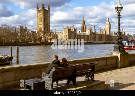 Couple sitting on a bench enjoying the view of london's historic parliament building along river thames Stock Photo