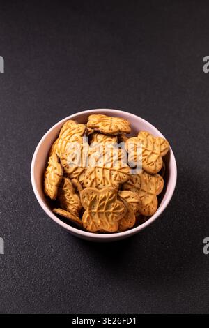 Leaf shaped cookies featuring chocolate filling are presented in a light pink ceramic bowl, placed on a dark, textured background, creating a simple y Stock Photo
