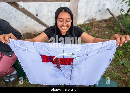 Aguacatan, Guatemala - A smiling young woman proudly displays a bright embroidered textile in a hoop while working outdoors, showcasing traditional cr Stock Photo