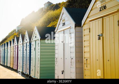 Pastel colored beach huts in a row with golden sunlight and green hillside, Bournemouth Dorset England Stock Photo