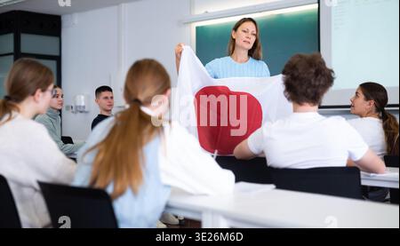 High school teacher tells students about Japan and holds a Japanese flag in hands. Stock Photo