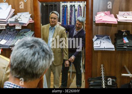 Tailor measuring a businessman's suit sleeve in a clothing store mirror Stock Photo
