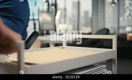 Close up of assistant pushing trolley cart with documents and folders from archive, bringing files to a colleague and ensuring efficient distribution of resources. Administrative tasks. Stock Photo