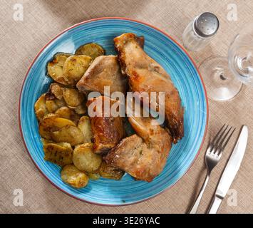 Roasted rabbit pieces with vegetable garnish of fried potatoes Stock Photo