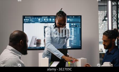 Black property developer discussing residential project investment and strategy for infrastructure growth and city planning in a bright office, analyzing blueprints and 3D models. Stock Photo