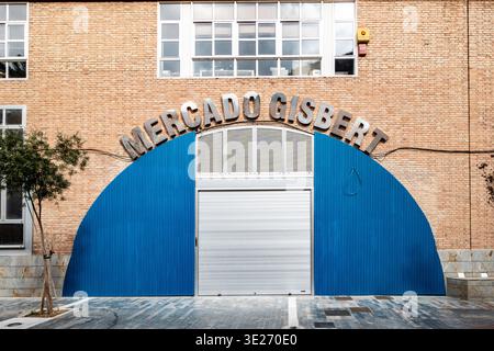 Mercado Gisbert entrance in Cartagena, Spain, featuring a large blue semicircular facade, silver metal lettering, and a closed roll-up shutter. Stock Photo