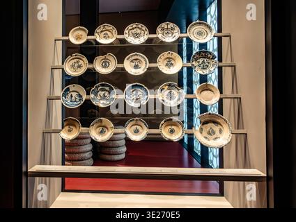 A display of blue and white ceramic plates at the Museo Foro Romano Molinete in Cartagena, Spain, arranged on tiered glass shelves. Stock Photo