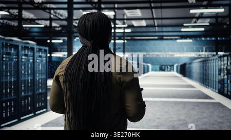 Data center system administrator monitors data center metrics on tablet to enhance operational effectiveness. IT expert in server room using analytics program to predict performance, camera A Stock Photo