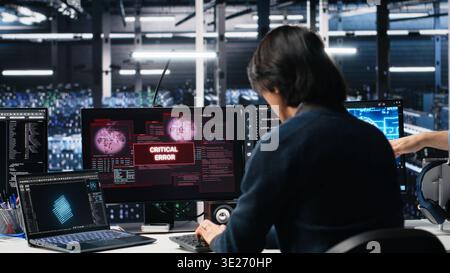 Data center team of engineers trying to fix critical error warning while using AI. Server farm teamworking colleagues repairing glitch popup while using artificial intelligence tech, camera A Stock Photo