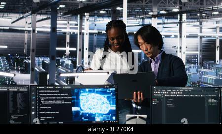 Data center engineers managing AI systems for uptime and efficiency, looking over paperwork files. African american woman and Asian man reading documents in multiethnic server hub, camera A Stock Photo