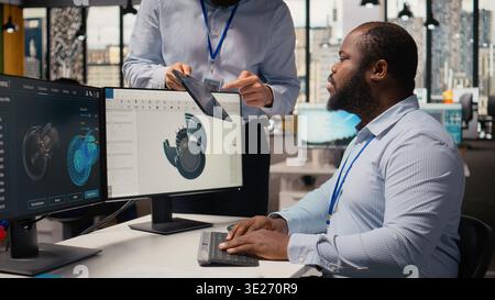Manager overseeing engineer using CAD app to optimize wind turbine design, reducing carbon footprint. RD office team leader and worker testing advanced materials for eco friendly windmill parts, camera A Stock Photo