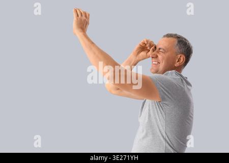 Mature man looking through imaginary spyglass on light background Stock Photo
