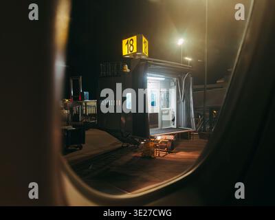 View from airplane window of illuminated jet bridge gate 18 at night, with terminal and ramp equipment Stock Photo