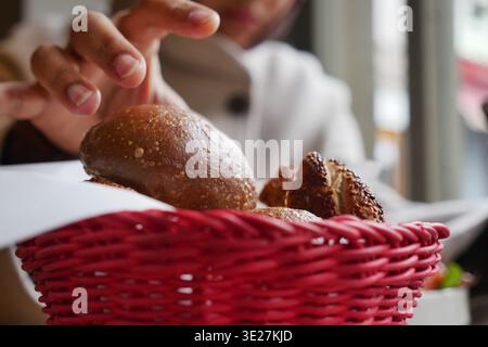 Hand reaches for bread rolls in a basket at a cafe Stock Photo