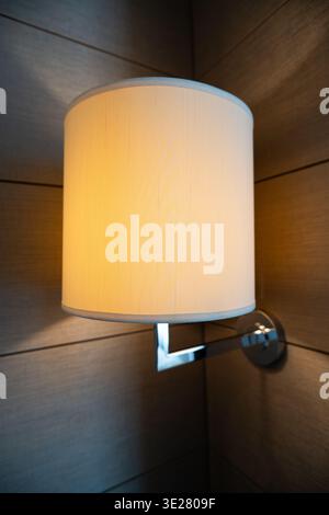 Modern wall lamp with white shade mounted on wooden panel wall in contemporary interior design Stock Photo