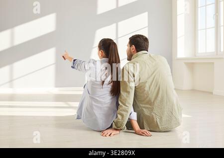 Happy married couple sitting on floor rear view, enjoying moving into new flat, planning renovation Stock Photo