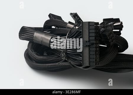 bundled black mesh-sleeved power cables isolated light gray background, 24-pin atx connector for psu or power supply unit wiring Stock Photo