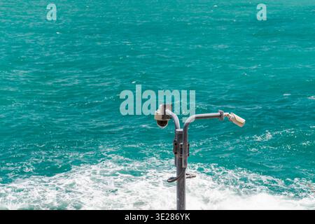 Security surveillance cameras on pole monitoring coastal area above turquoise sea Stock Photo