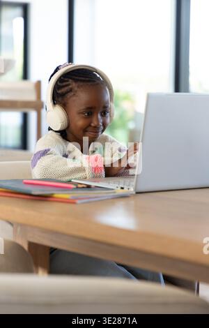 African American female child sitting at wood table at home using laptop with notebooks nearby Stock Photo