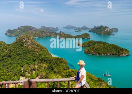 Middle-aged woman standing on scenic viewpoint overlooking tropical islands and turquoise sea, peaceful travel moment in coastal national park Stock Photo