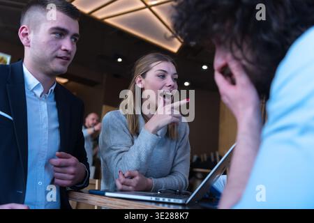 Happy young couple and friends having fun while working together on laptop in a modern cafe. Lifestyle, teamwork, communication and startup business c Stock Photo
