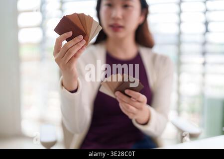 Adult Asian female thoughtfully examining various wood color swatches. Professional choosing material for home decor renovation design project. Stock Photo