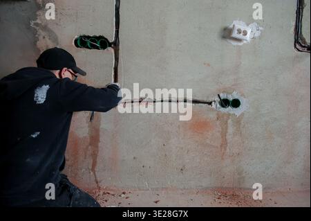 Professional electrician stretches wires in a new apartment. Installation of wiring in a room. Installation of a switchboard in a new building. Repair Stock Photo