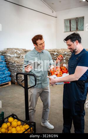Warehouse workers discussing produce quality holding fresh tomatoes Stock Photo