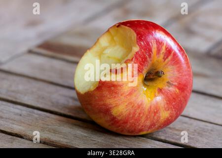 Nutrition, table and bitten apple in home for healthy snack, fresh produce and vitamin C. Wellness, vegan and fruit on wooden surface in kitchen for Stock Photo