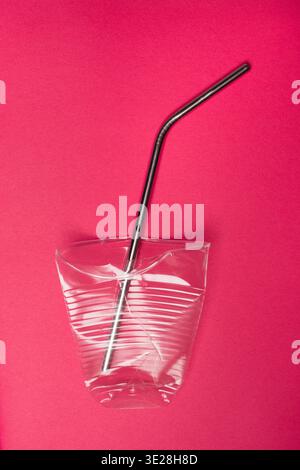 Conceptual Shot of a Reusable Metal Straw inside a Crushed Single-Use Plastic Cup on a Vibrant Red Background Stock Photo