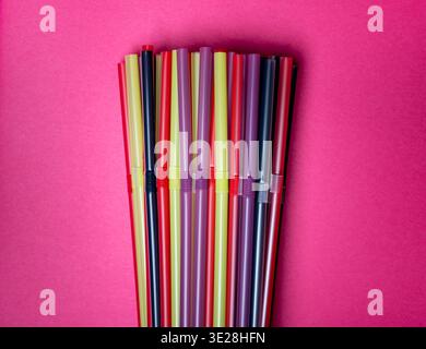 Bundle of Multi-Colored Plastic Drinking Straws on a Vivid Pink Background Stock Photo