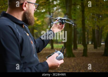 Man holds flying drone and controls it with remote. Bearded man operating quadcopter in a park, testing flight and monitoring performance, concept of modern technology and hobby Stock Photo