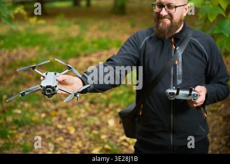Man holds hovering drone while controlling it with remote. Bearded man catching quadcopter in park during flight, combining control and handling, concept of modern technology and hobby Stock Photo