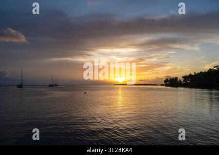 A beautiful sunset over Tahaa Island in French Polynesia, with calm waters and sailboats creating a serene atmosphere Stock Photo