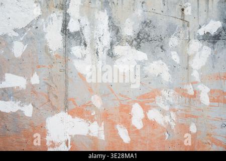 Grungy concrete wall texture with white and orange paint splatters and weathered cement surface. Stock Photo